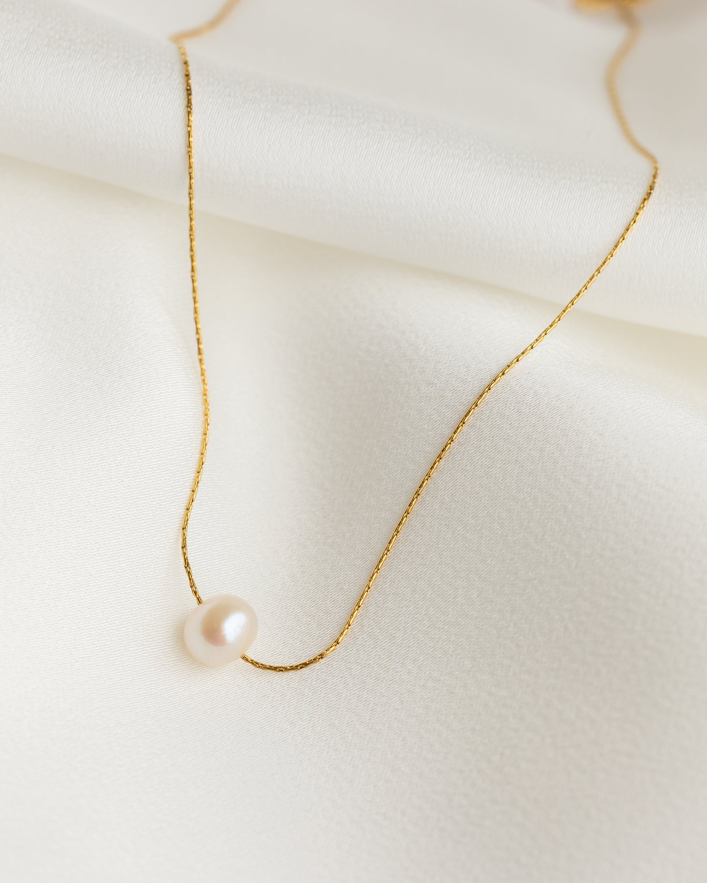 Delicate gold necklace with a single pearl on a light background
