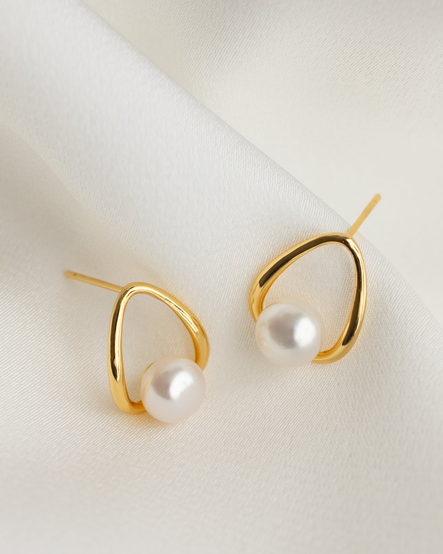 Gold earrings with pearls on a light background