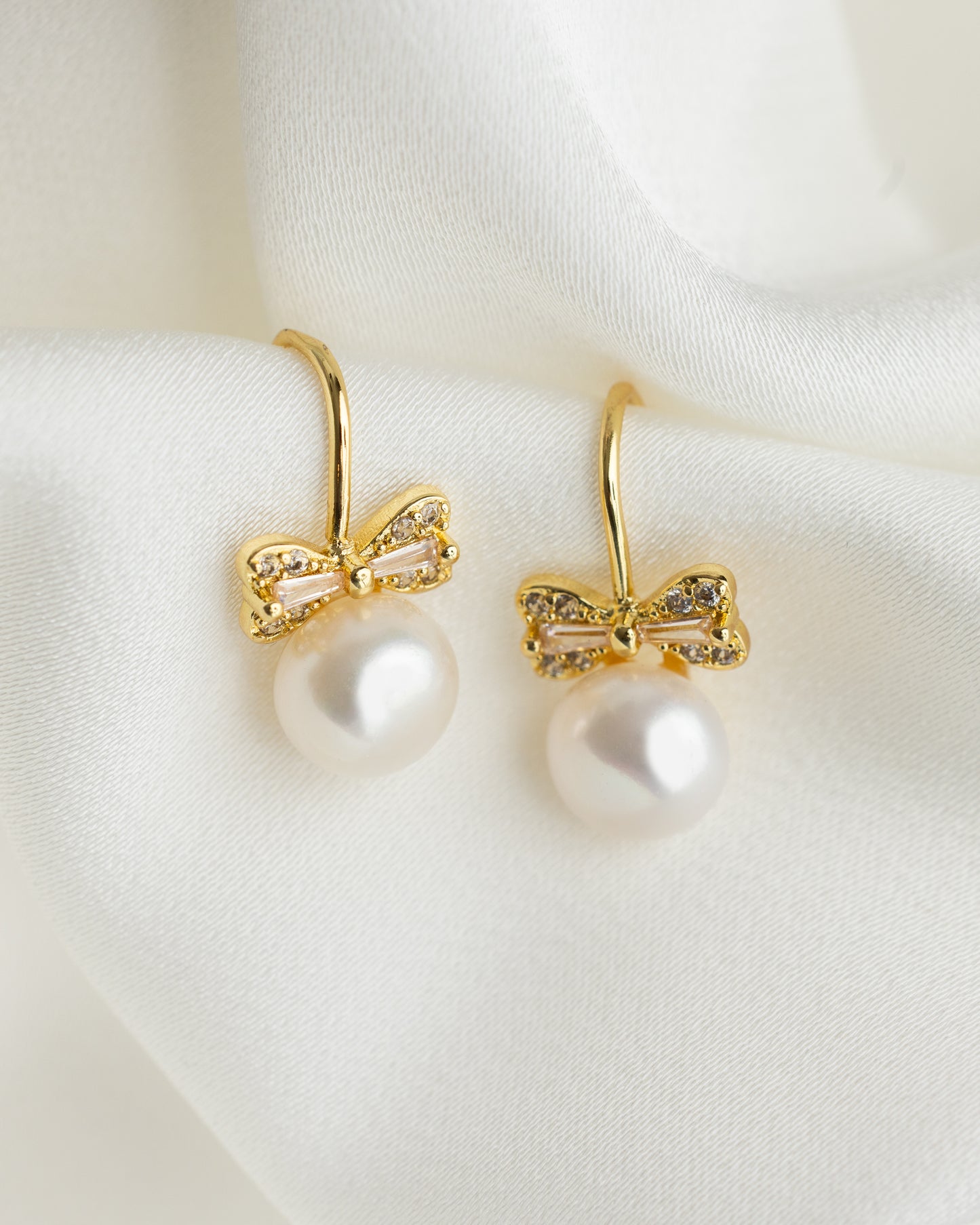Gold bow earrings with pearl centers on a white fabric background