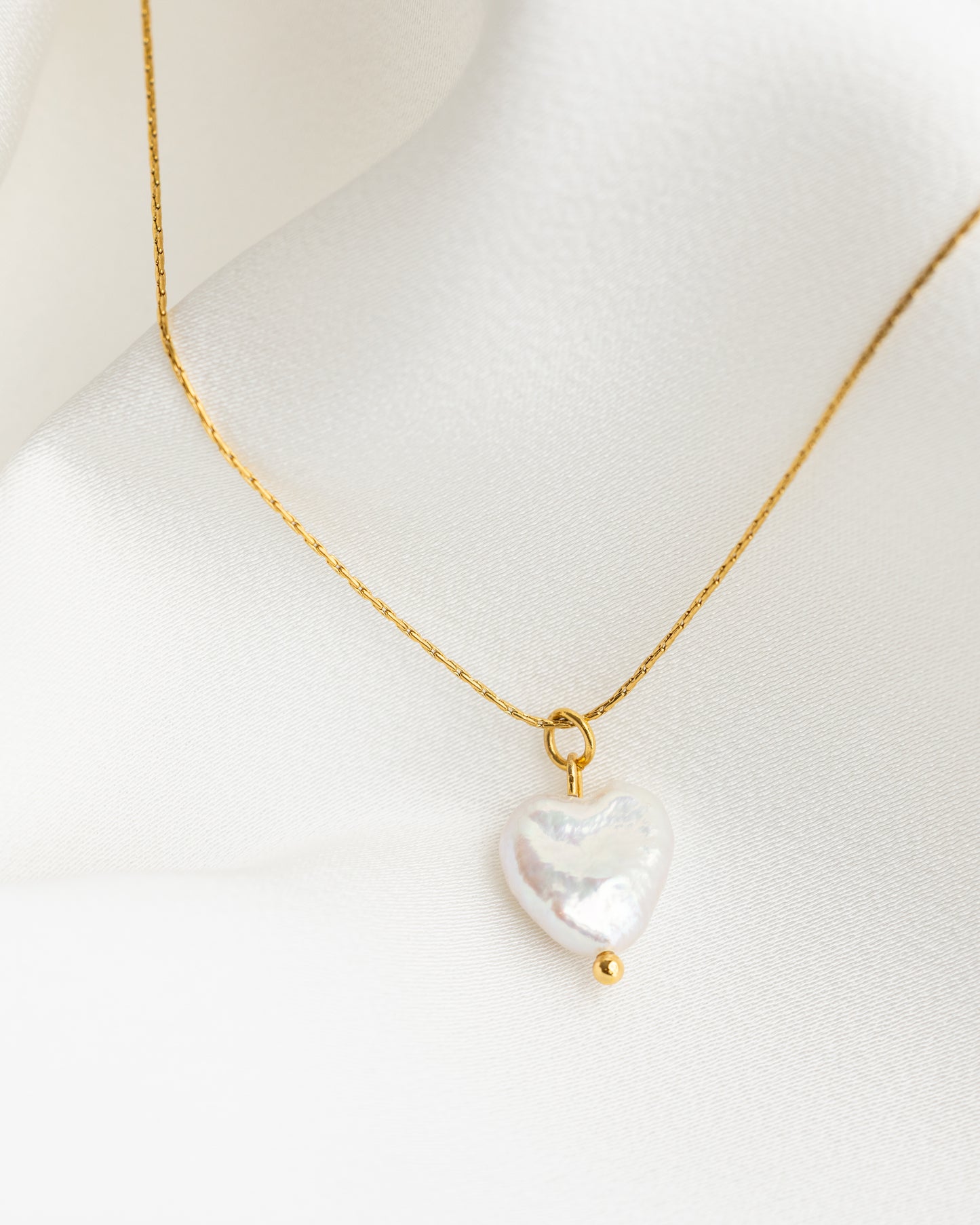 Gold necklace with a heart-shaped pearl pendant on a mannequin.