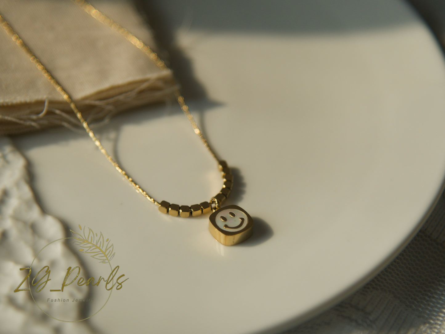 Gold necklace with a smiley face pendant on a textured surface, featuring the brand 'Zg Pearls'.