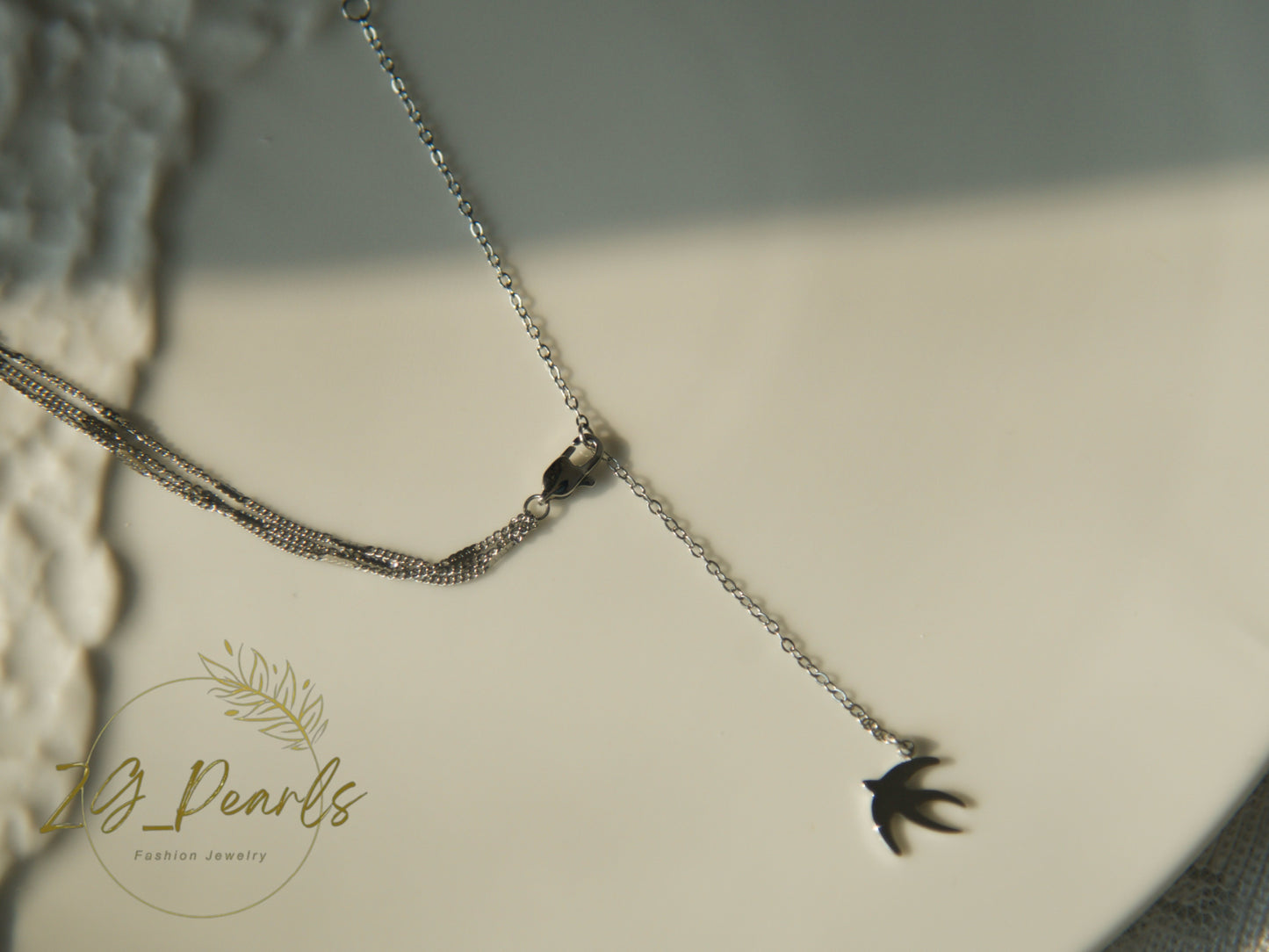 Necklace with a bird-shaped pendant on a neutral background, featuring the brand 'ZG Pearls'.