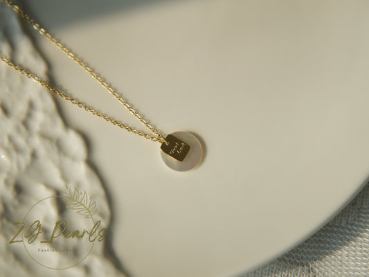 Gold necklace with a hexagonal pendant on a textured surface, featuring the brand 'ZG Pearls'.