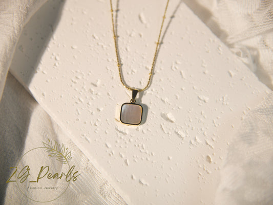 Necklace with a pendant on a textured beige surface, featuring the brand 'zg Pearls'.