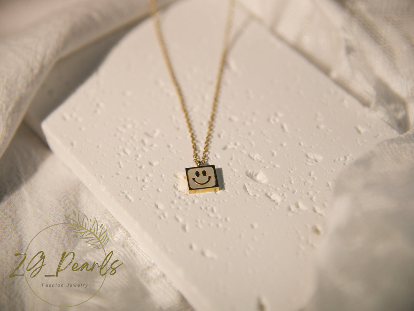 Necklace with a smiley face pendant on a textured surface, featuring the brand 'Zg Pearls'.