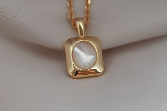 Gold necklace with a pendant on a beige fabric background