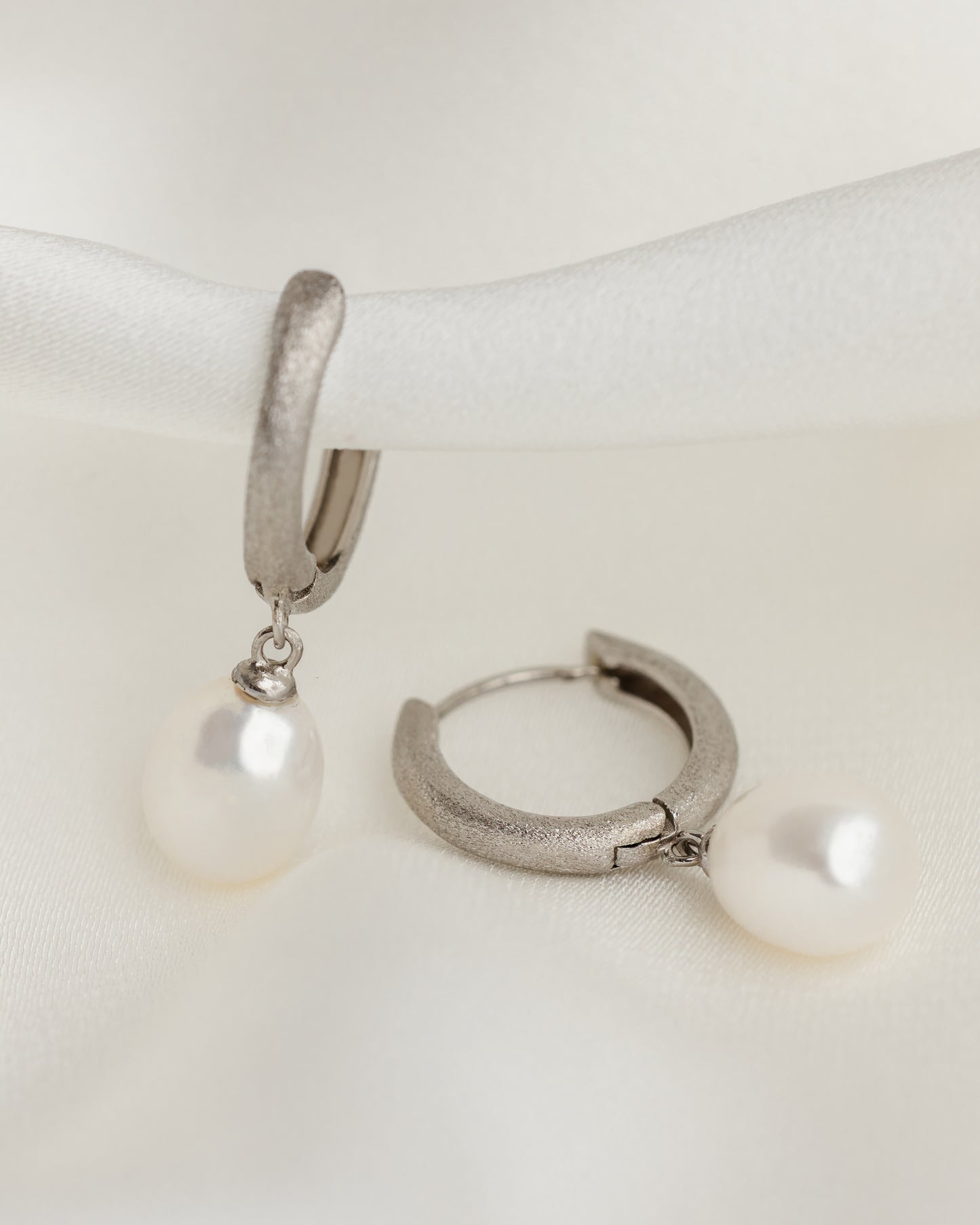 Silver hoop earrings with pearl drops on a white surface