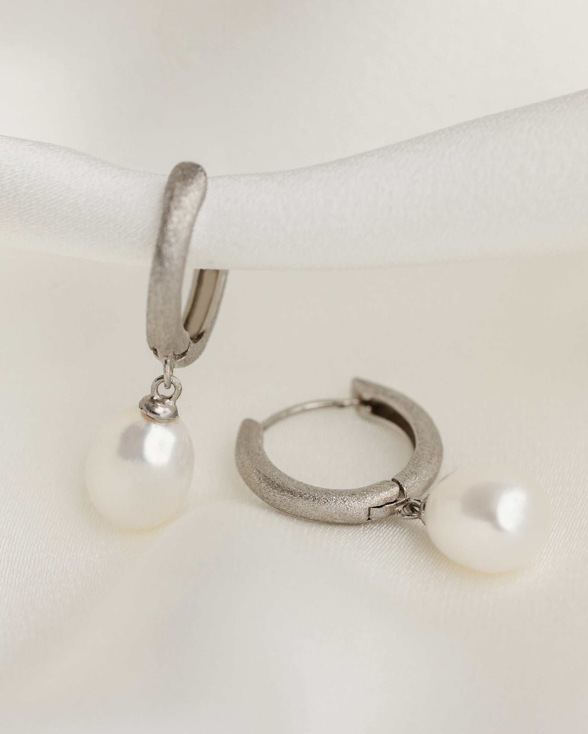 Silver hoop earrings with pearl drops on a white surface