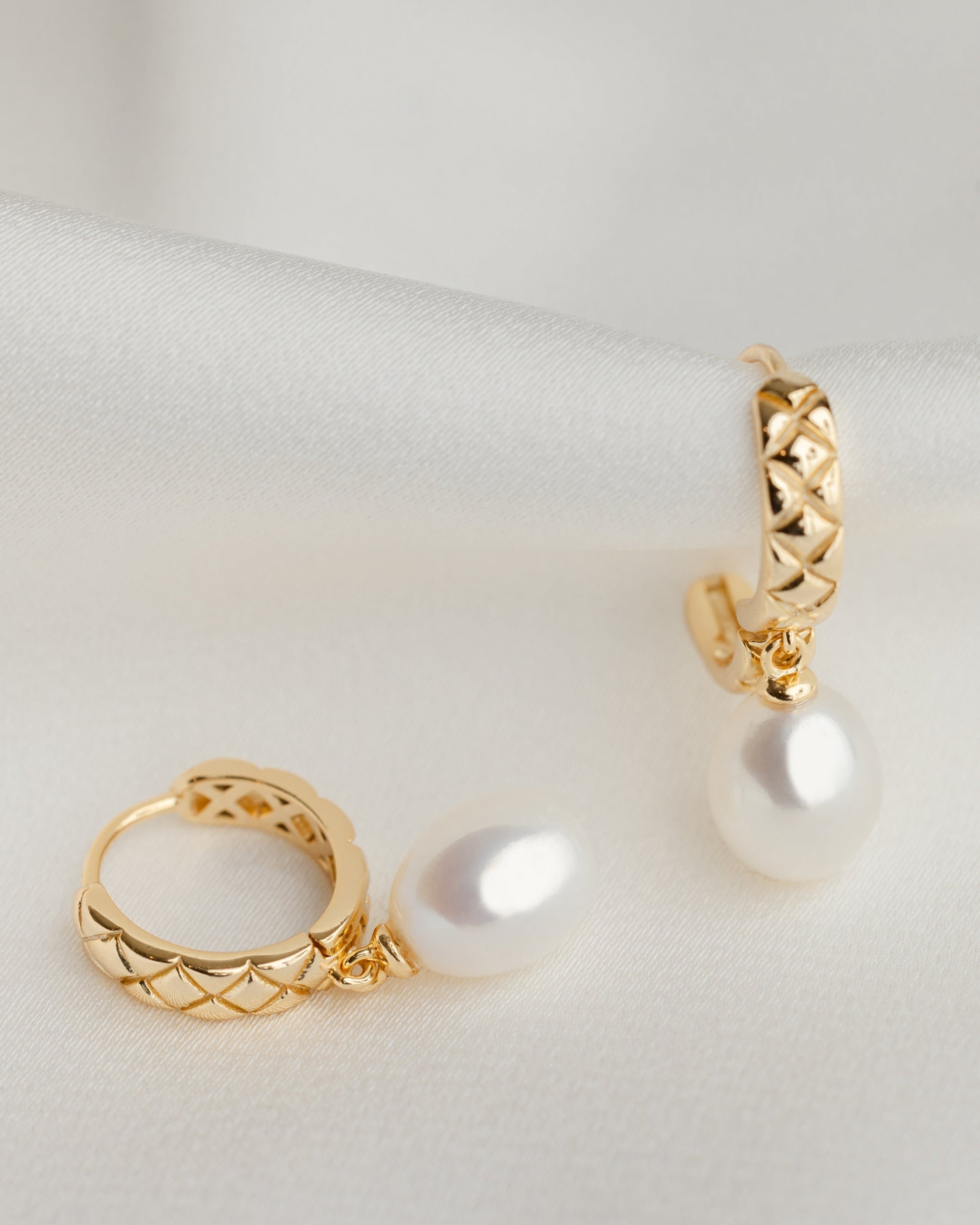 Gold hoop earrings with pearl drops on a light gray background