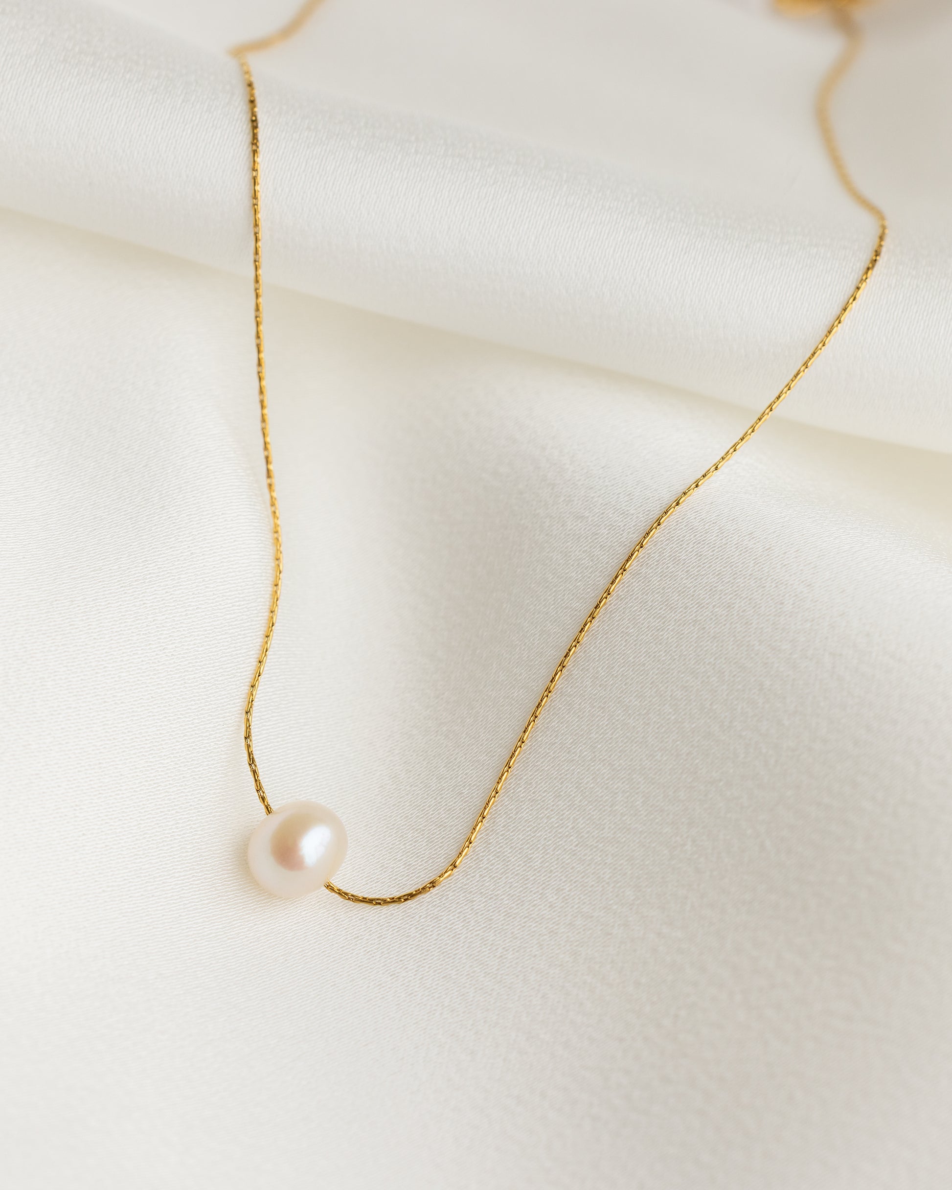 Delicate gold necklace with a single pearl on a light background