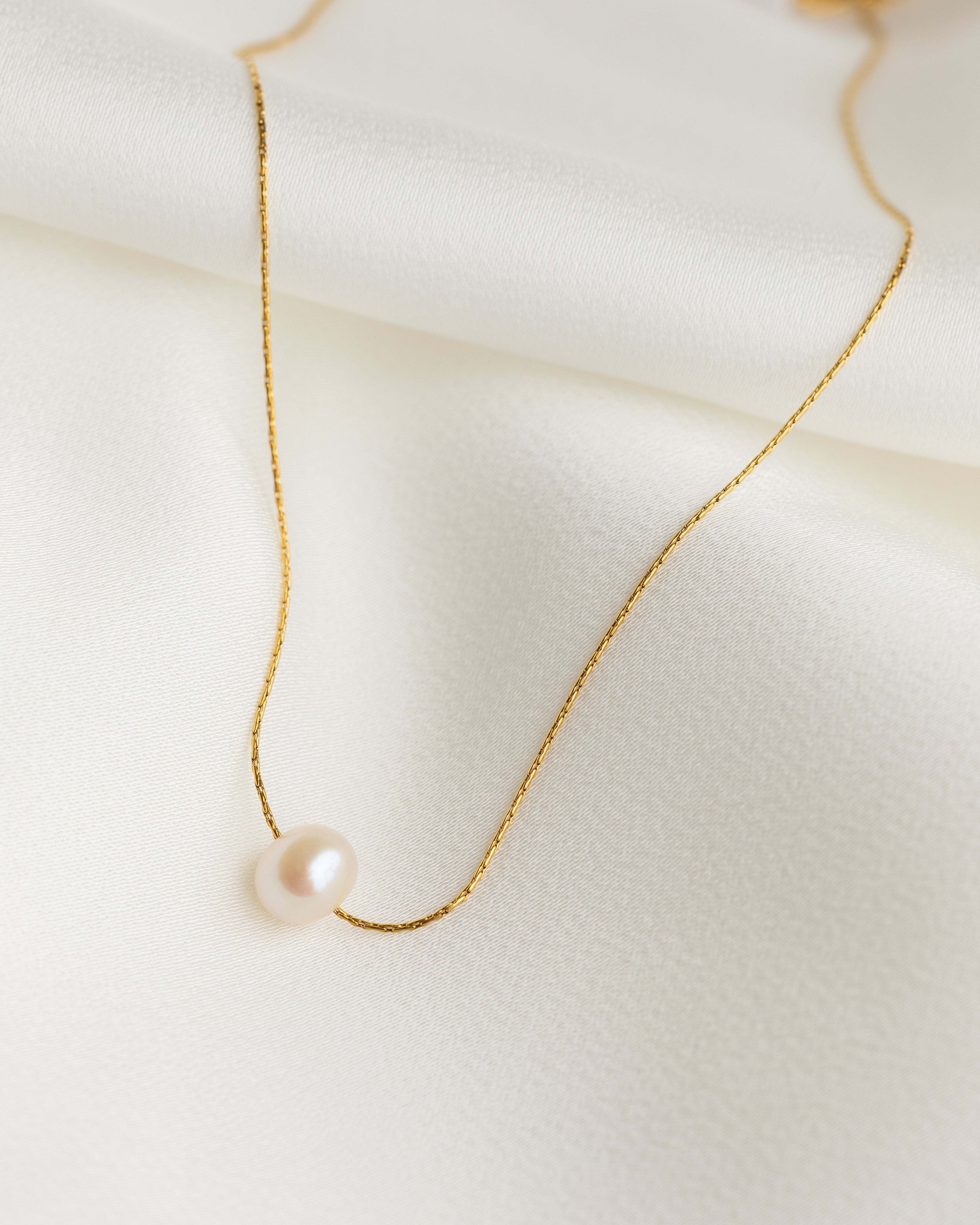 Delicate gold necklace with a single pearl on a light background