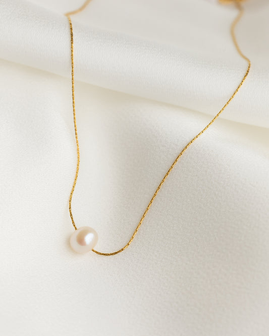 Delicate gold necklace with a single pearl on a light background