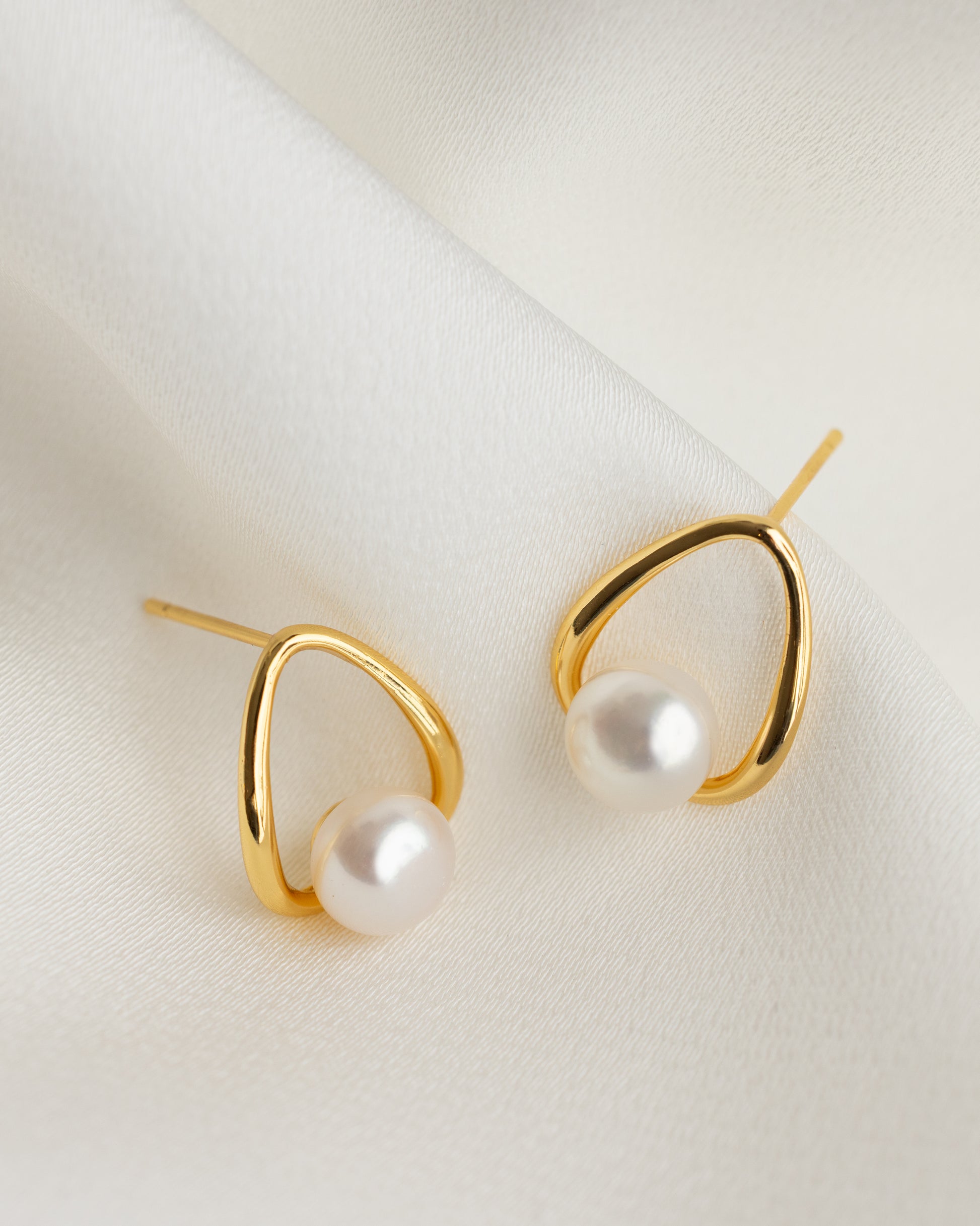 Gold earrings with pearls on a light background