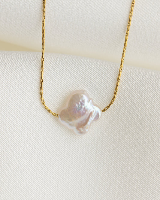Gold necklace with a large pearl pendant on a white background