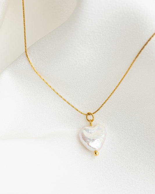 Gold necklace with a heart-shaped pearl pendant on a mannequin.