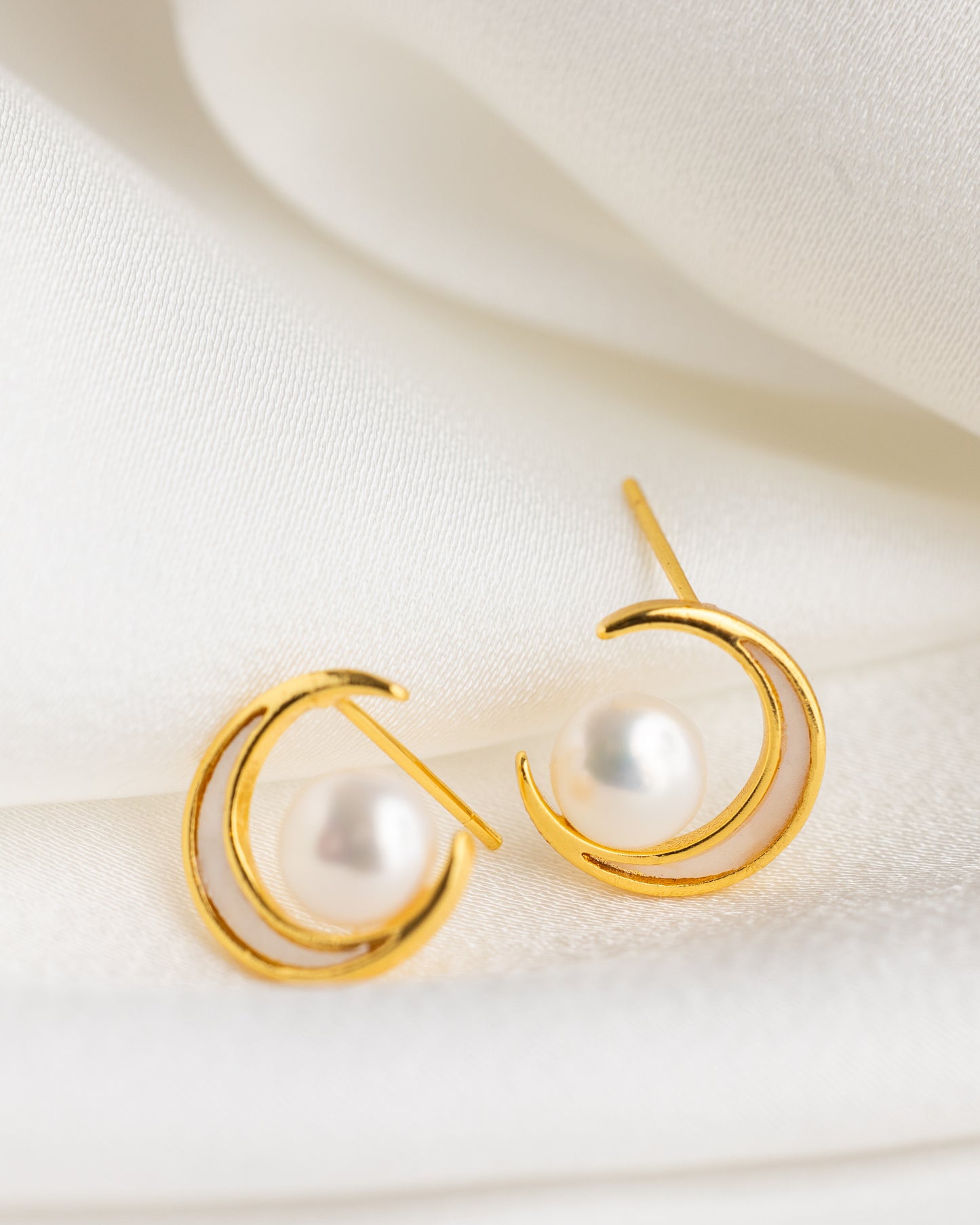 Gold earrings with pearl-like centers on a white fabric background