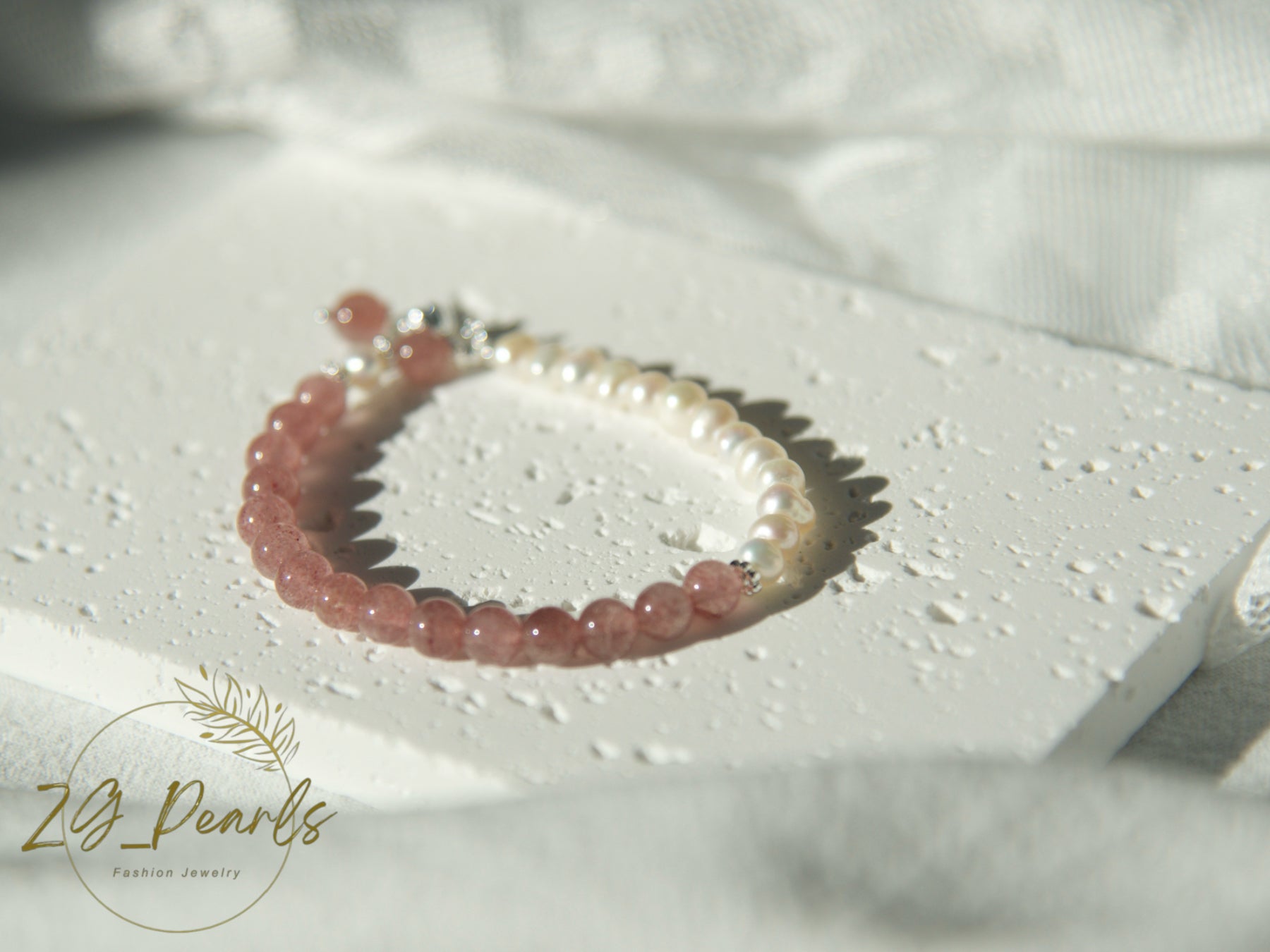 a pearl bracelet with pink strawberry crystal on a textured white surface with 'Zg Pearls' branding.