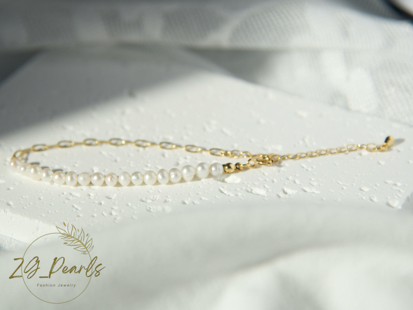 Gold chain necklace with pearls on a white fabric background, featuring the ZJ Pearls brand.