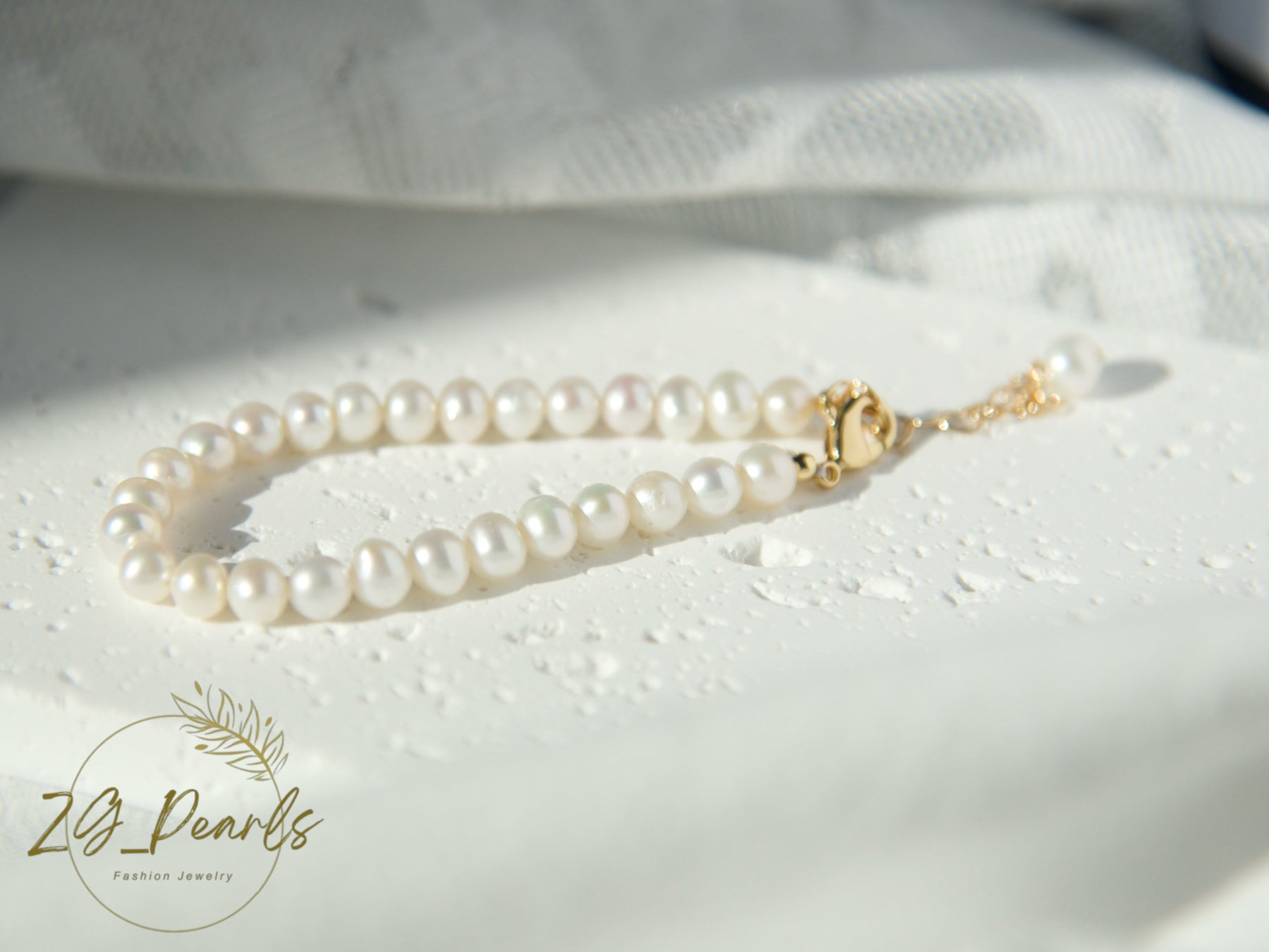 Pearl necklace with a gold clasp on a textured white surface, featuring the Zg Pearls logo.