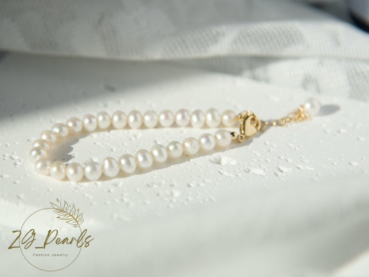 Pearl necklace with a gold clasp on a textured white surface, featuring the Zg Pearls logo.