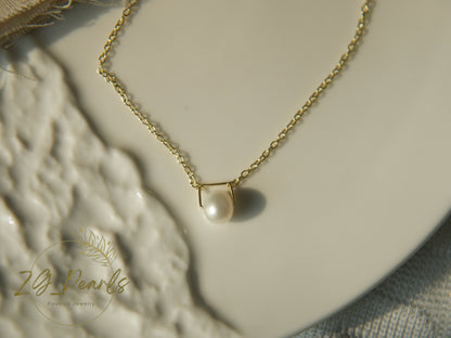 Gold necklace with a pearl pendant on a textured surface, featuring the brand 'ZG Pearls'.