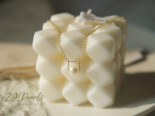 Necklace with a pearl pendant on a textured white block, branded 'zG Pearls'.