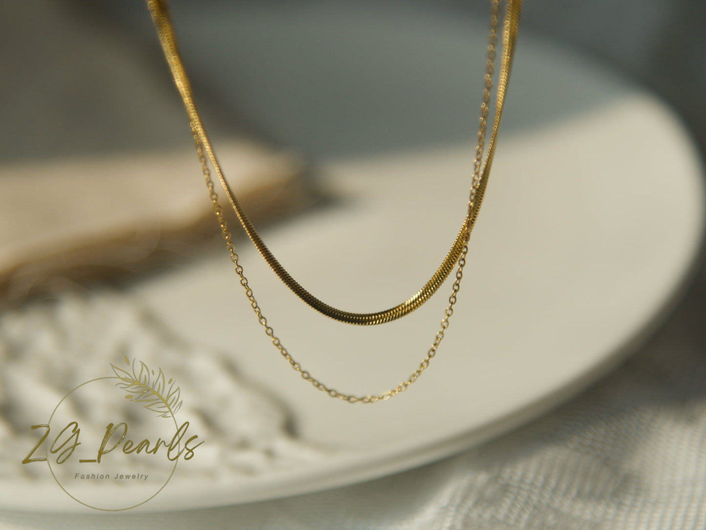 Gold necklace on a white plate with '2B Pearls' branding.