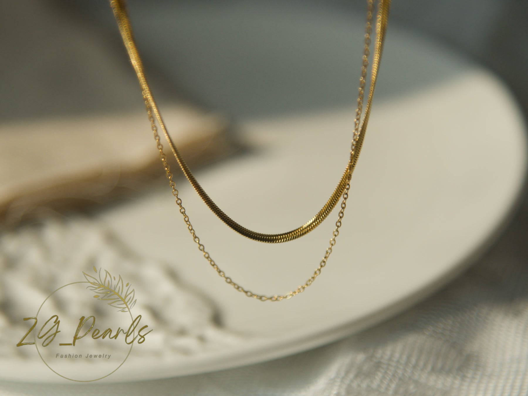 Gold necklace on a white plate with '2B Pearls' branding.