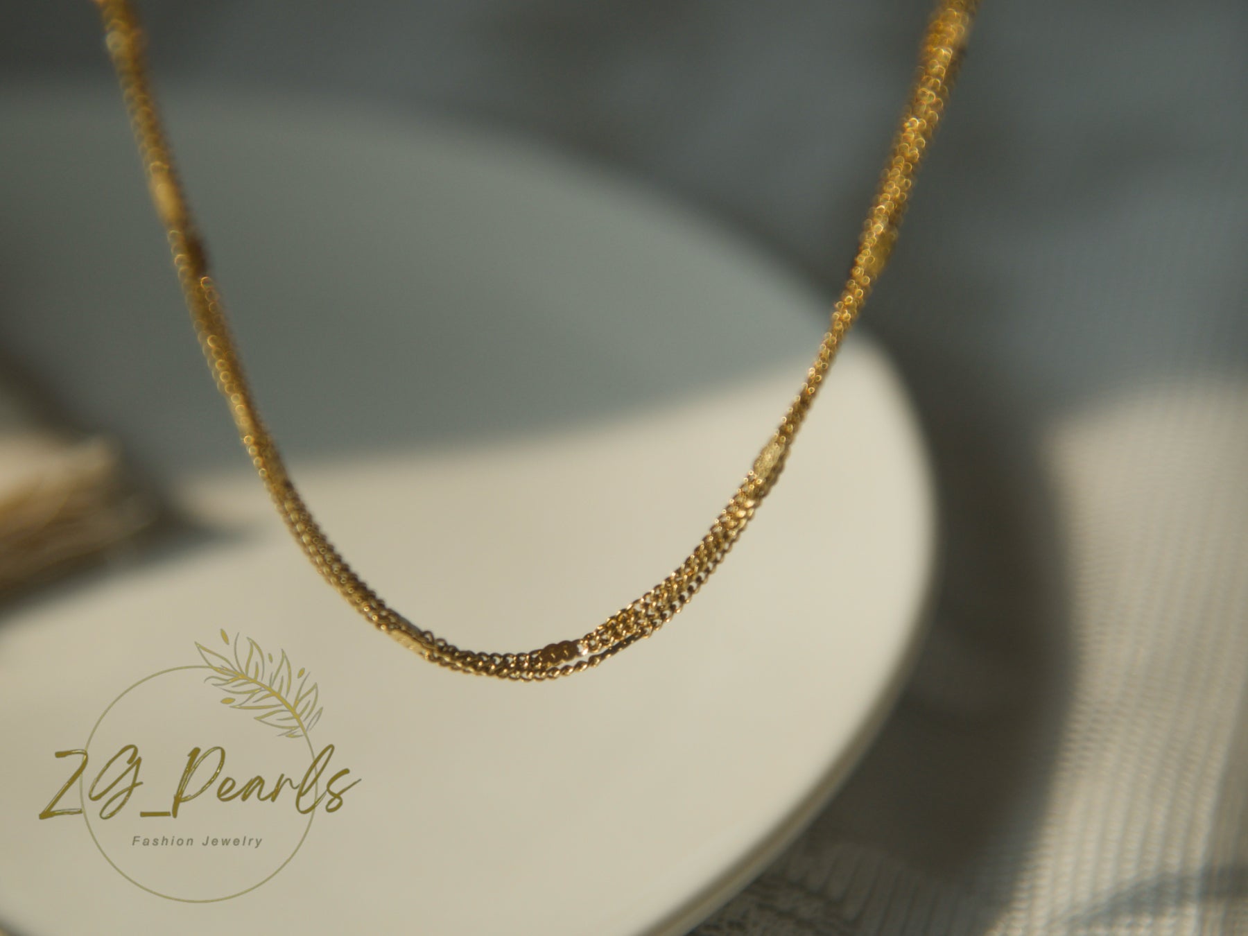 Gold necklace on a white stand with 'ZG Pearls' branding.