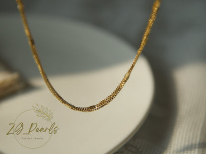 Gold necklace on a white stand with 'ZG Pearls' branding.