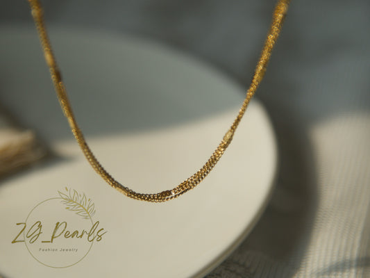 Gold necklace on a white stand with 'ZG Pearls' branding.