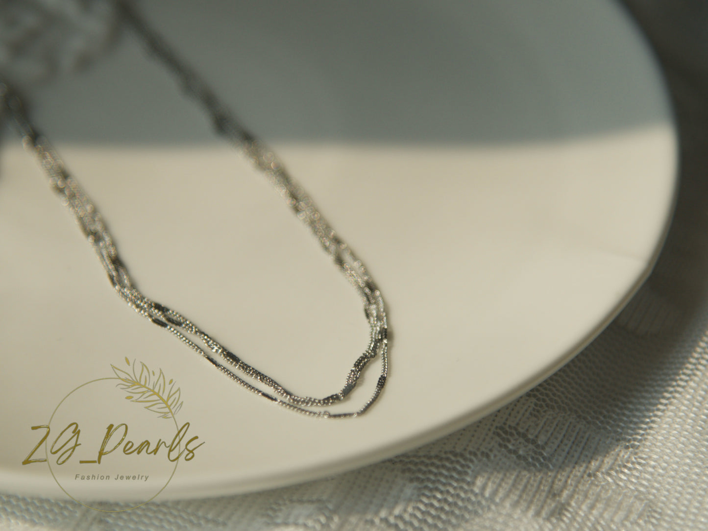 Silver necklace on a white plate with 'ZG Pearls' branding.
