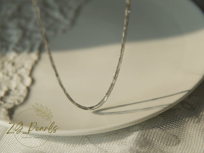 Silver necklace on a textured surface with 'ZG Pearls' branding.