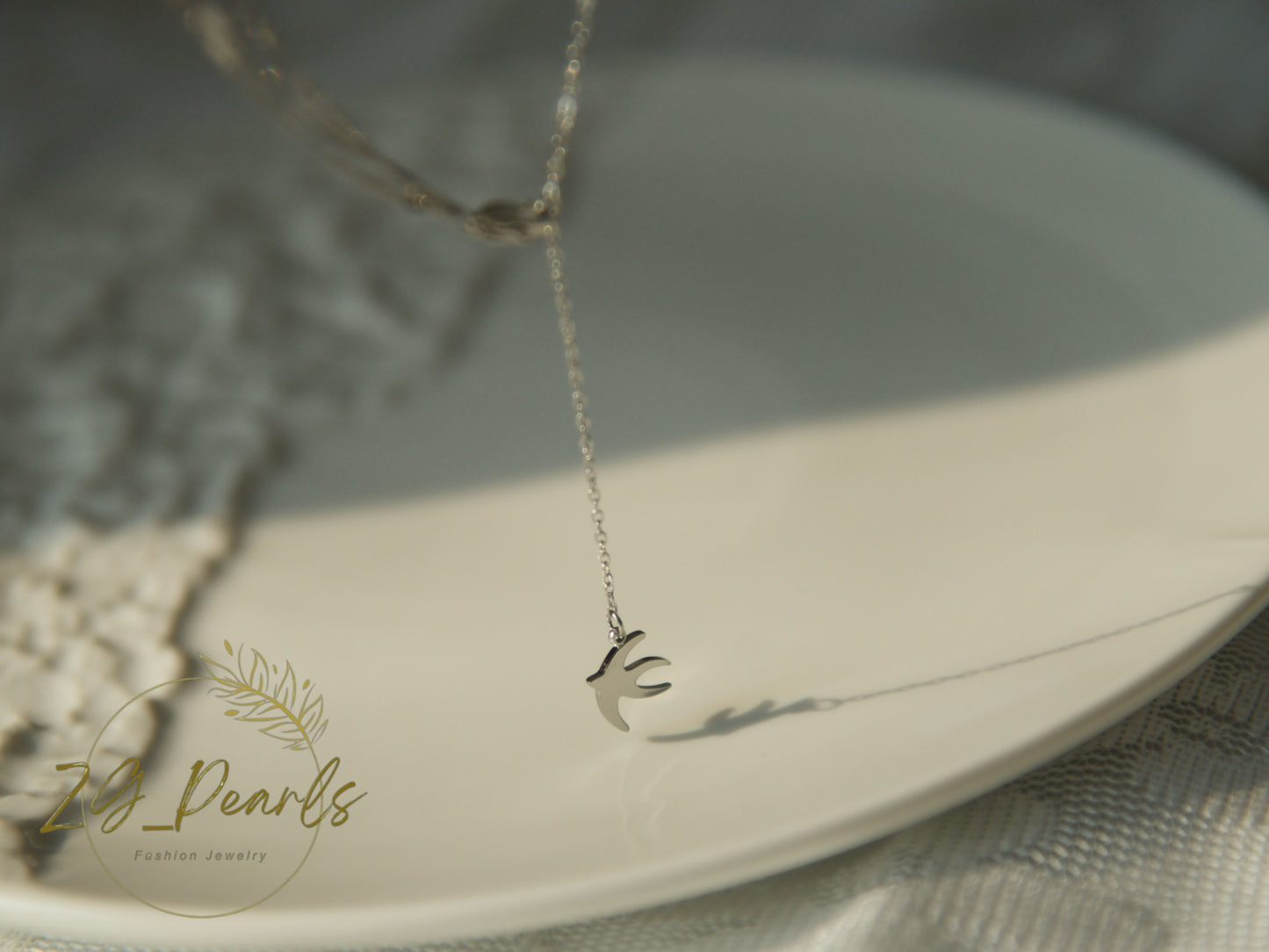 Silver necklace with a bird pendant on a white plate, branded 'ZG Pearls'.