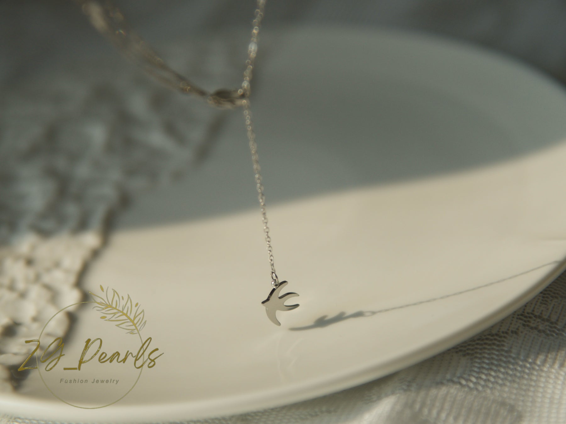 Silver necklace with a bird pendant on a white plate, branded 'ZG Pearls'.