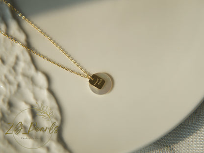 Gold necklace with a hexagonal pendant on a textured surface, featuring the brand 'ZG Pearls'.