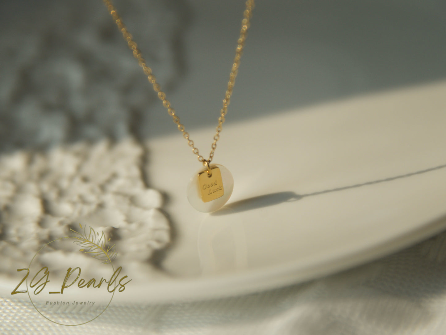 Gold necklace with a pendant on a white surface, featuring the brand 'ZG Pearls'.