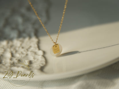 Gold necklace with a pendant on a white surface, featuring the brand 'ZG Pearls'.