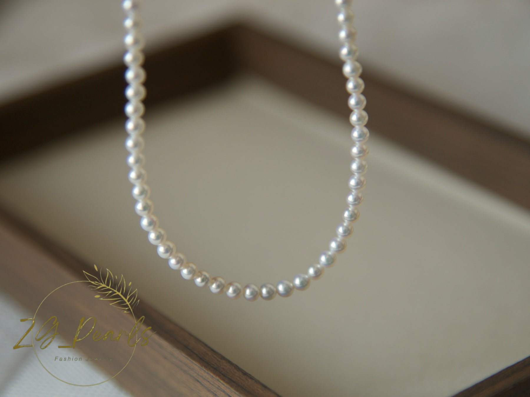 Pearl necklace on a neutral background with a brand logo in the corner.