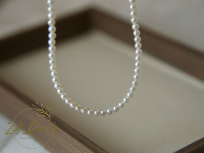 Pearl necklace on a neutral background with a brand logo in the corner.