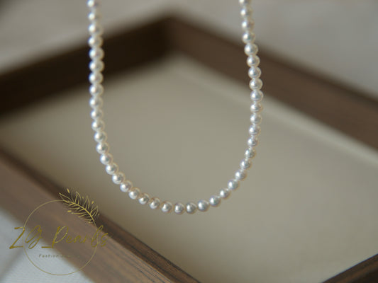 Pearl necklace on a neutral background with a brand logo in the corner.