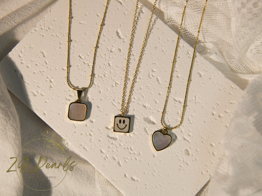 Three gold necklaces with unique pendants on a textured beige surface, featuring the brand 'ZG Pearls'.