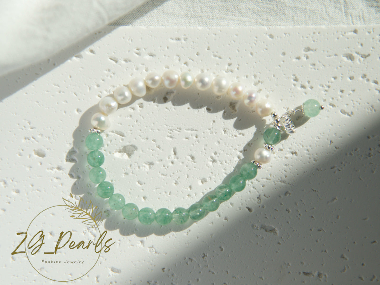 Pearl and green bead bracelet on a textured surface with 'ZG Pearls' branding.