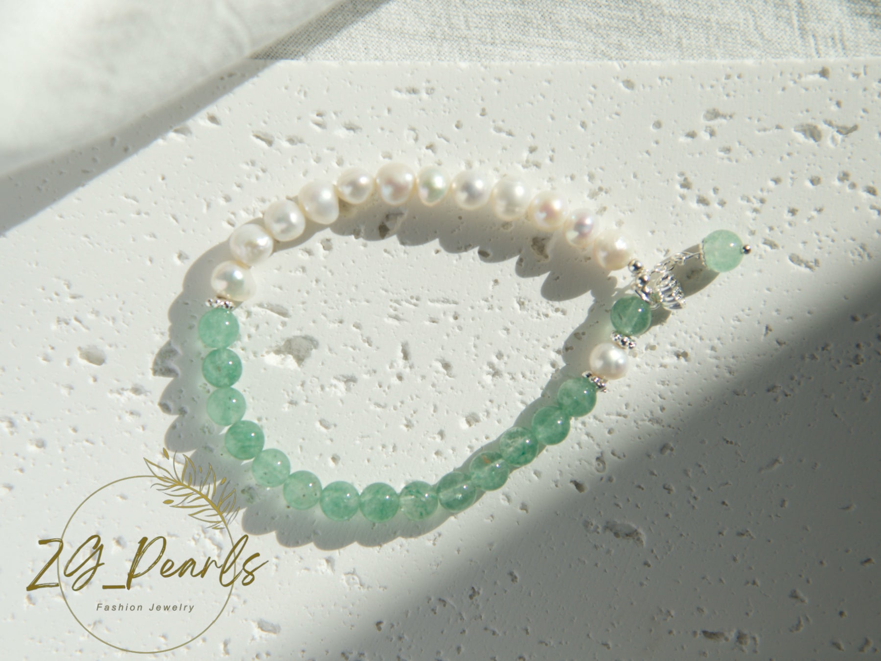 Pearl and green bead bracelet on a textured surface with 'ZG Pearls' branding.