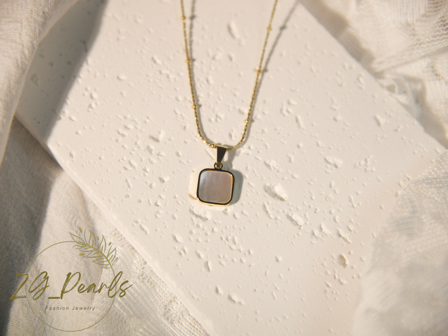 Necklace with a pendant on a textured beige surface, featuring the brand 'zg Pearls'.
