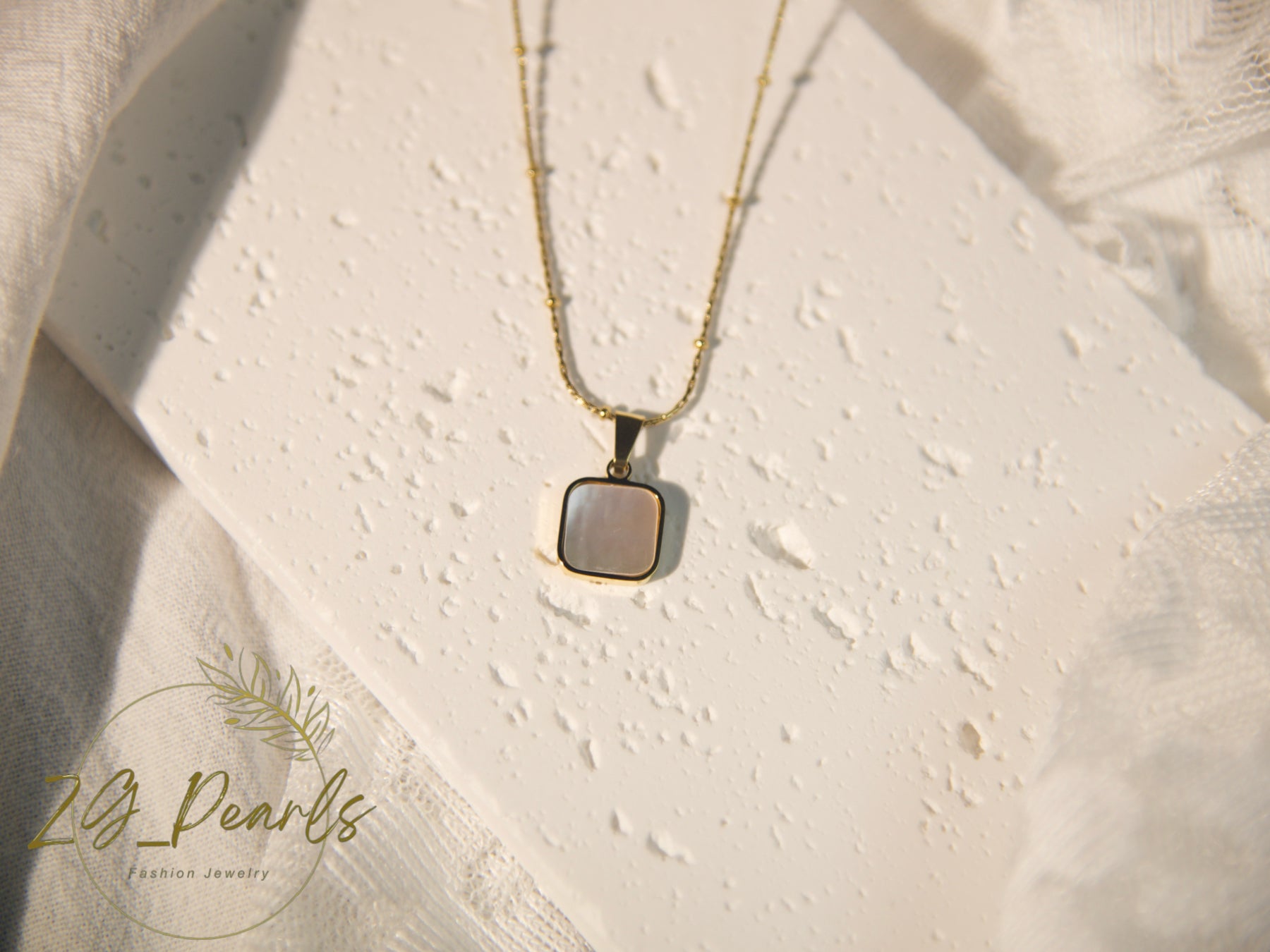 Necklace with a pendant on a textured beige surface, featuring the brand 'zg Pearls'.