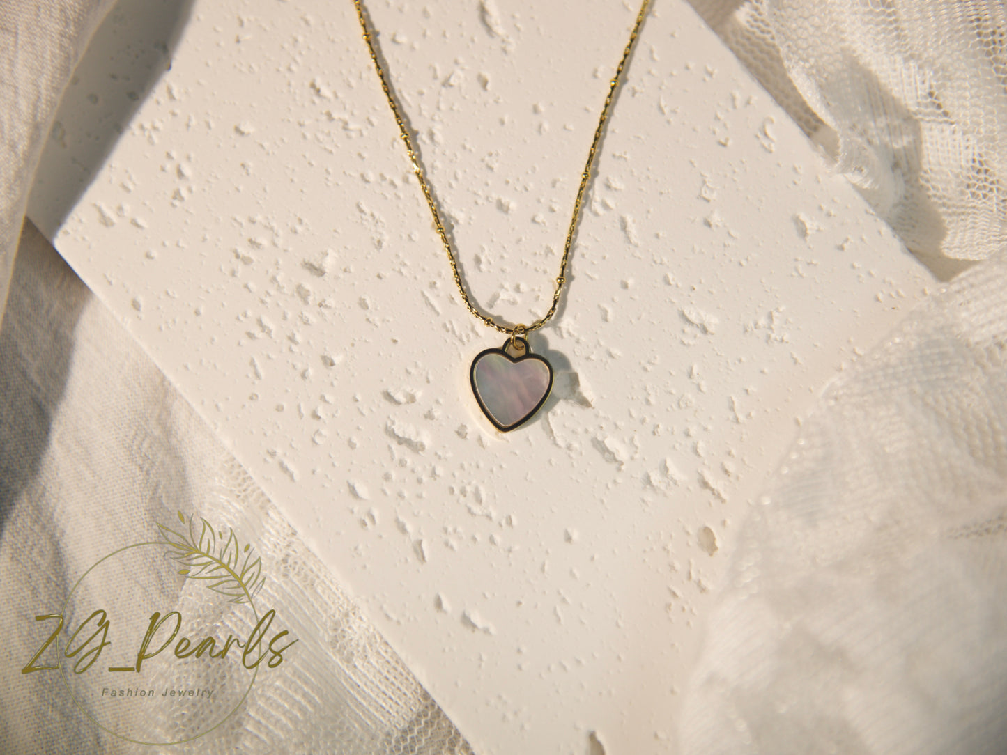 Necklace with a heart-shaped pendant on a textured beige background, featuring the brand 'ZB Pearls'.
