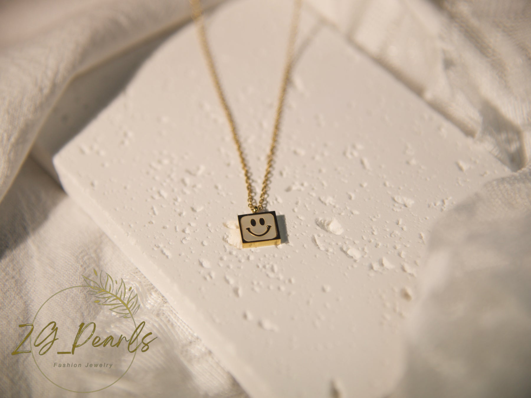 Necklace with a smiley face pendant on a textured surface, featuring the brand 'Zg Pearls'.