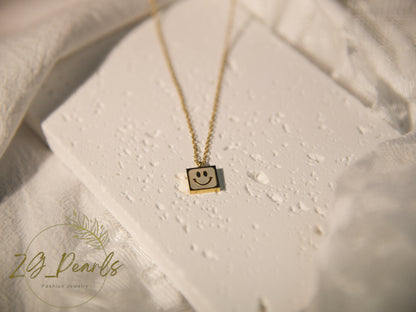 Necklace with a smiley face pendant on a textured surface, featuring the brand 'Zg Pearls'.