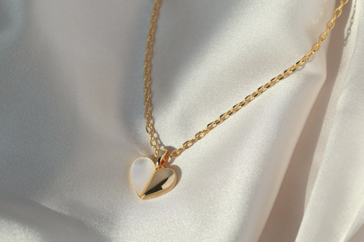 Gold necklace with a heart-shaped pendant on a white fabric background